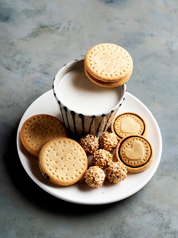 Oatmeal cookies with sesame seeds and flax seeds with a glass of milk on a gray background.