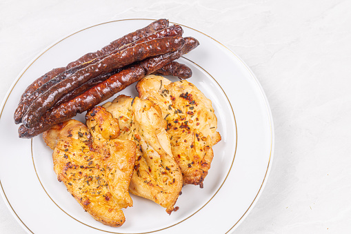 Delicious chicken breasts fried and served with fried sausages on the plate.