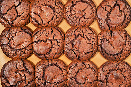 Freshly baked chocolate cookies on a baking sheet with a lining. Top view of brownie cookies, image for banner or background