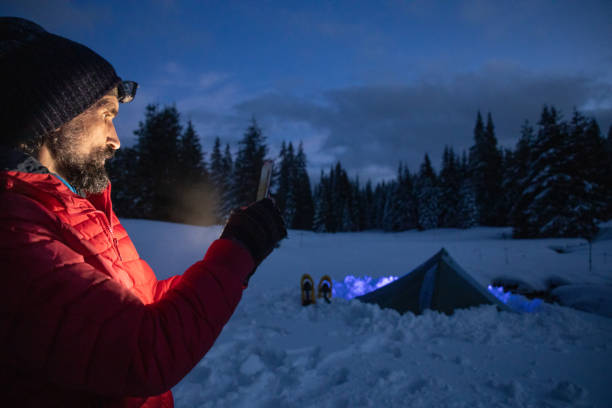 istock Tourist using phone near tent at night while camping in winter mountain. Alone in nature while COVID-19 pandemic. Mental health and life balance. 1313148523