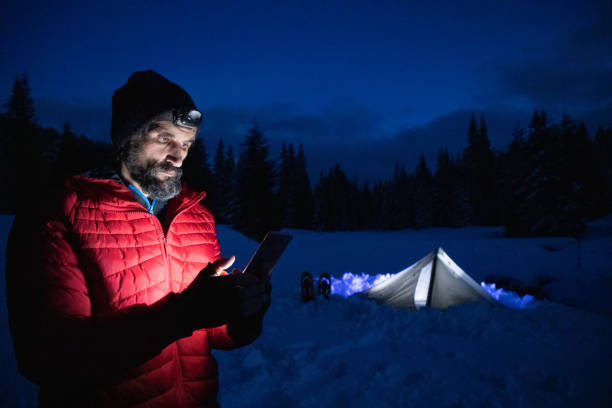 istock Tourist using phone near tent at night while camping in winter mountain. Alone in nature while COVID-19 pandemic. Mental health and life balance. 1313148533