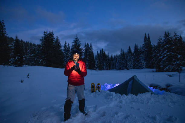 istock Tourist using phone near tent at night while camping in winter mountain. Alone in nature while COVID-19 pandemic. Mental health and life balance. 1313148536