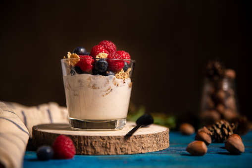 Glass of homemade granola with yogurt and fresh raspberries, hazelnut and blueberries on blue wooden background. Fitness breakfast. Space for text on dark background.