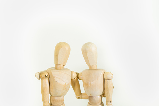 Two wooden artist's drawing doll friends with their arms around each other in cooperation on a white background with copy space.
