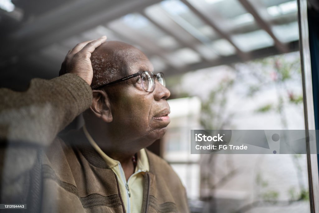 Worried senior man looking through the window at home Alzheimer's Disease Stock Photo