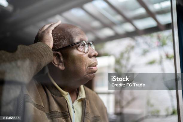 Worried Senior Man Looking Through The Window At Home Stock Photo - Download Image Now