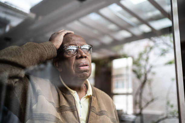 hombre mayor preocupado mirando a través de la ventana en casa - pensive senior adult looking through window indoors fotografías e imágenes de stock