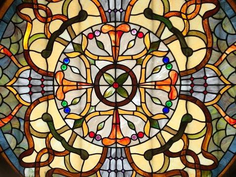 Small detail of a generic Art Nouveau style stained glass window. Yellow orange and red tones, with blue and green floral notes.