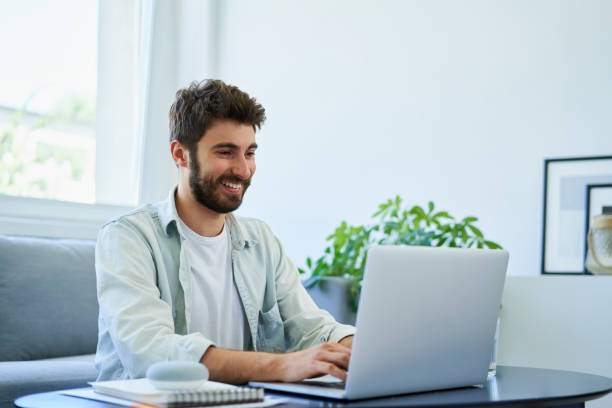 junge glückliche mann tippt auf laptop während der arbeit zu hause. gutes haltungskonzept - gute haltung stock-fotos und bilder