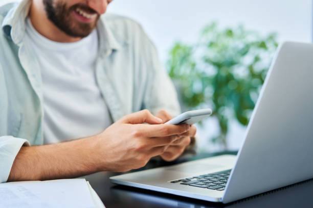 istock Closeup of happy man texting on mobile phone smartphone while using laptop 1313158495