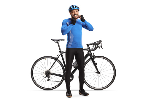 Full length portrait of a male cyclist putting on a helmet and smiling next to his bicycle isolated on white background