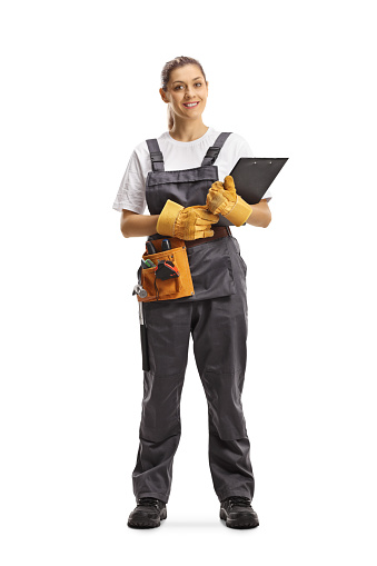 Full length portrait of a young repairwoman with a tool belt holding a clipboard isolated on white background