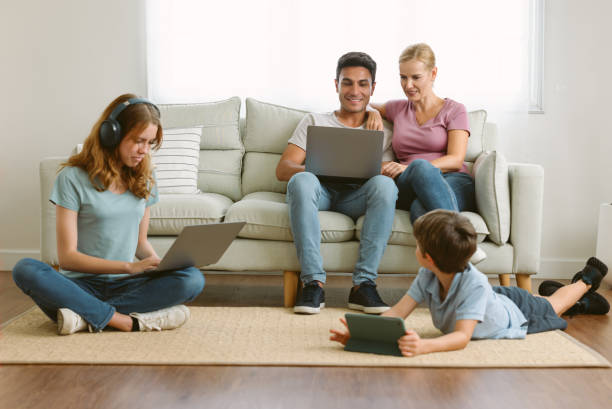 Stay at home caucasian parents working on laptops while sit on sofa and son lying on the floor watching cartoon on tablet and teenage daughter studying with laptop doing online research homework. quédense en casa padres caucásicos trabajando en computadoras portátiles mientras se sientan en el sofá y el hijo acostado en el suelo viendo dibujos animados en la tableta y la hija adolescente estudiando con computadora portátil haciendo tareas de i