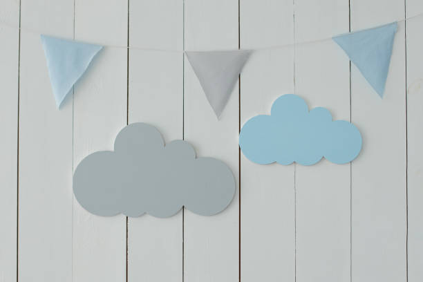 istock White wall is decorated with multi-colored garland of flags and decorative clouds. Decor for holiday. Stylish children room with hanging flags. Decoration for baby room. Baby Shower party. Kid Holiday 1313168189