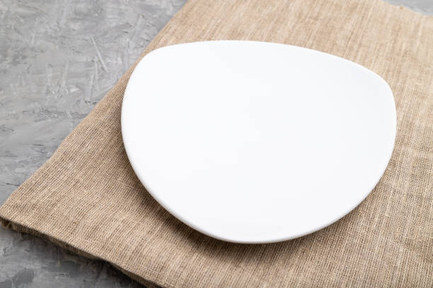 istock Empty white plate on gray concrete background and linen textile. Side view, close up. 1313170153