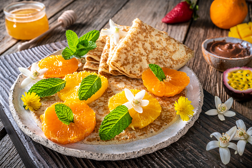 Citrus Crepes arrangement with fruits, berries, cocoa cream and varied vegetarian food still life on rustic wood