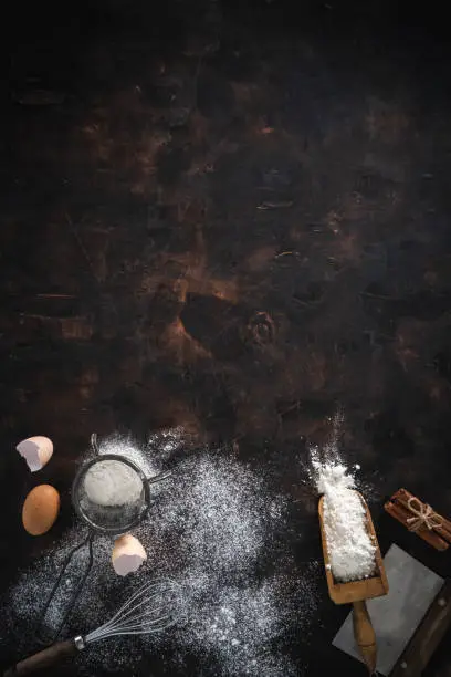 Photo of Bakery background with flour, eggs, sieve, whisk, serving scoop, cinnamon and Bench Scraper