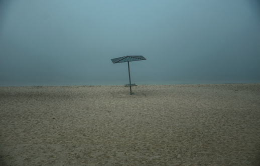 empty sandy beach and lonely parasol. Foggy weather in England. Background and texture. End of the tourist season on the coast