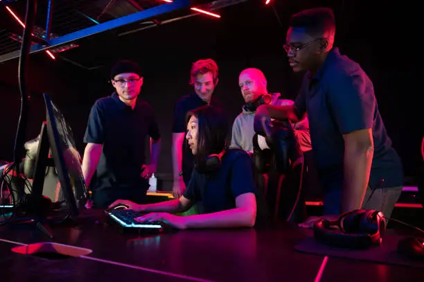 Photo of During a training session before the Dota 2 championship, the coach explains their strategy to the team, the girl plays at the computer