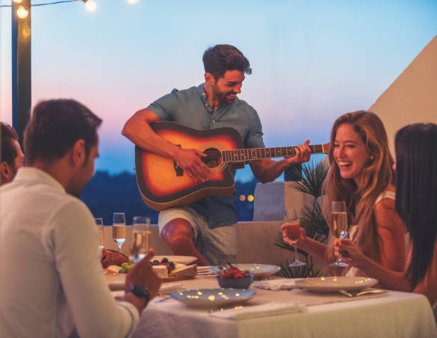 Group of friends having a dinner party with one man playing guitar.