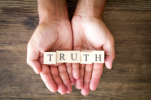 Truth written on small wooden blocks, held in a man's hands. 
Shot from above on a wooden background. Stock photo.