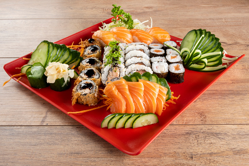 Mixed sushi roll and salmon sashimi on red plate.
