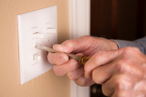 Worker or homeowner installing or repairing switch plates and plugs on wall.