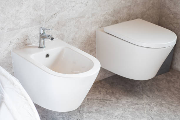 bidet bianco appeso a parete e servizi igienici su piastrelle di ceramica grigia in bagno - bidet foto e immagini stock