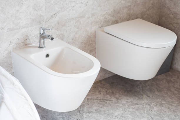 biały bidet wiszący na ścianie i toaleta na szarych płytkach ceramicznych w łazience - bidet zdjęcia i obrazy z banku zdjęć