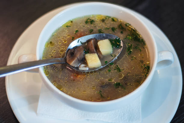 istock Lean mushroom soup. Spoon with broth, mushrooms and potatoes, in deep white bowl 1313192873