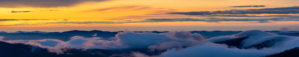 A vibrant sunrise fills the sky as fog rolls through the valley creating a cloud inversion along the Blue Ridge Parkway in Western North Carolina.