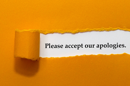 Por favor, acepte nuestras disculpas escritas bajo papel naranja roto photo