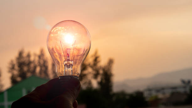 istock Solar power in nature concept light bulb hand held background with sunset evening 1313205456