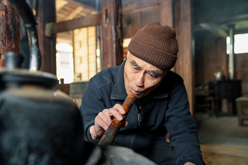 Senior Japanese man cooking on wood burning stove. Kamikatsu, Japan