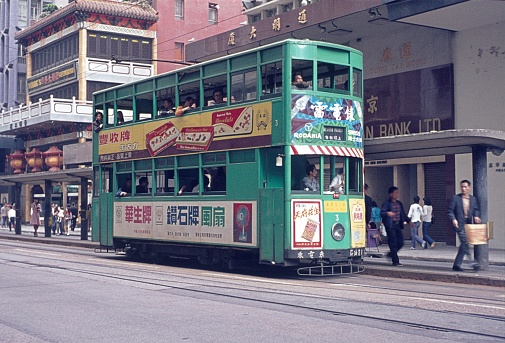Hong Kong, China, 1974. The unique Hong Kong tram at a stop. Also: passengers, passers-by and buildings.