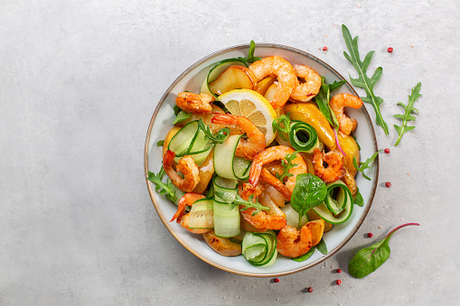 Fresh salad with grilled prawns, caramelized pears, cucumber and mixed greens, with lemon dressing.  Light grey background. Top view.