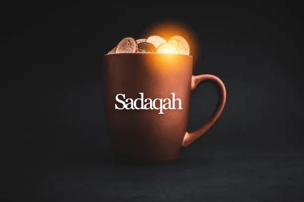 SADAQAH or Charity Gift text with Coins in cups on black background. Charity Concept
