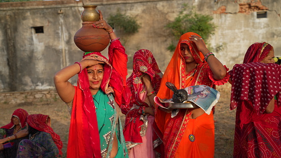 08 April 2021- Reengus, Sikar, India. Two Hindu cultured women with ornamented clothes with a clay pot. Second female holding a sacred plate of Bhog in her hand.