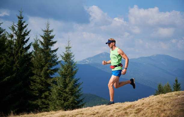 Professional runner training run downhill in the mountains. Professional young blond athlete running trail on grassy downhill of mountains in summer sunny day. Beauty mountain landscape on background. beskid mountains photos stock pictures, royalty-free photos & images