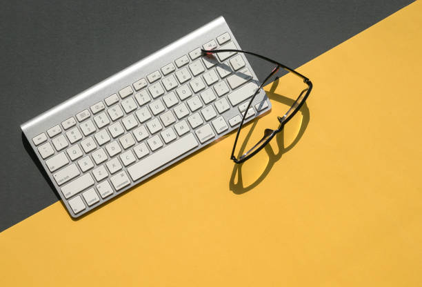 istock White keyboard and reading glasses on yellow and black background top. 1313230151