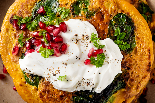 Gluten free recipe for red lentil pancakes; red lentils soaked overnight and blended, chickpea flour, chilli powder, cumin, tumeric, greek yoghurt, spinach leaves, spring onions and fresh coriander.  Served with more yoghurt, fresh parsley and pomegranate seeds. Overhead view, horizontal format with some copy space