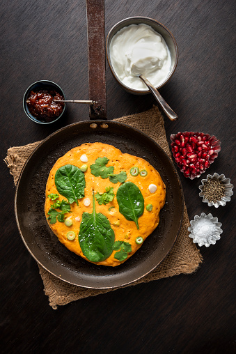 Gluten free recipe for red lentil pancakes; red lentils soaked overnight and blended, chickpea flour, chilli powder, cumin, tumeric, greek yoghurt, spinach leaves, spring onions and fresh coriander.  Served with more yoghurt, fresh parsley and pomegranate seeds. Overhead view, vertical format with some copy space