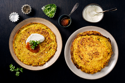 Gluten free recipe for red lentil pancakes; red lentils soaked overnight and blended, chickpea flour, chilli powder, cumin, tumeric, greek yoghurt, spinach leaves, spring onions and fresh coriander.  Served with more yoghurt, fresh parsley and pomegranate seeds and chutney. Overhead view, horizontal format with some copy space