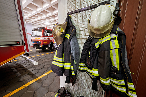 Firefighter’s turnout jackets and helmets hanging near fire engines parked in station garage for quick access when responding to an emergency.