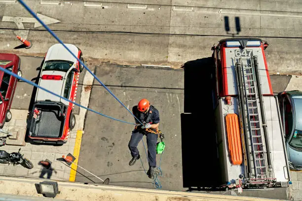 Photo of High Angle View of Male Firefighter Rappelling Down Building