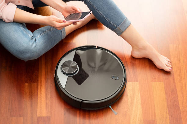 Faceless middle section of young woman using automatic vacuum cleaner to clean the floor, controlling smart machine housework robot with smart phone Faceless middle section of young woman using automatic vacuum cleaner to clean the floor, controlling smart machine housework robot with smart phone mop photos stock pictures, royalty-free photos & images