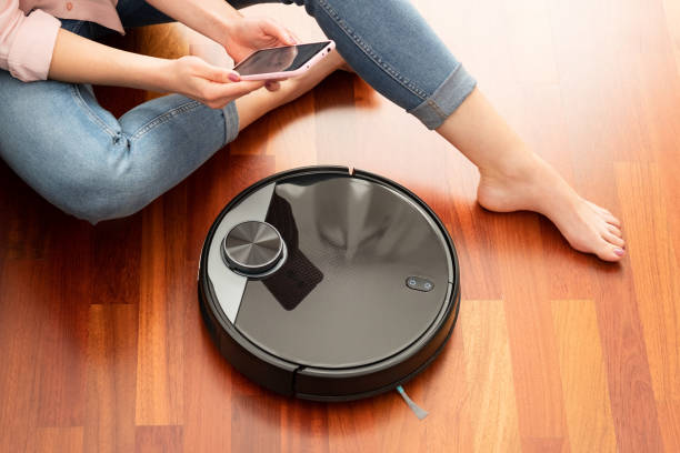 faceless middle section of young woman using automatic vacuum cleaner to clean the floor, controlling smart machine housework robot with smart phone - domestic car color image horizontal car imagens e fotografias de stock