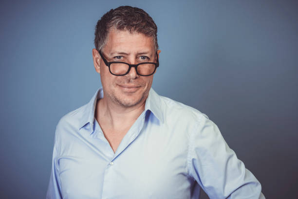 istock Middle aged man with black glasses and blue shirt posing against blue background 1313234331
