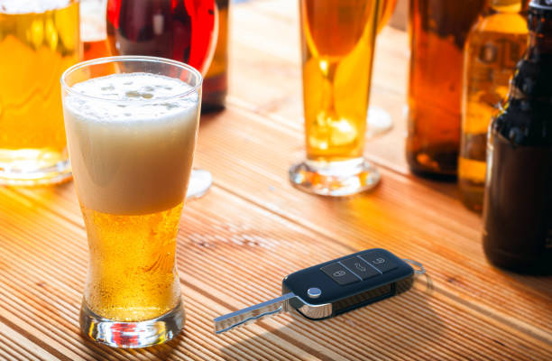 Drinking and driving concept. Car key and alcohol glass on wooden background. 3d illustration. Drinking and driving concept. Car key and beer glass on a wooden pub counter background. 3d illustration. pics of drunk driving accidents stock pictures, royalty-free photos & images