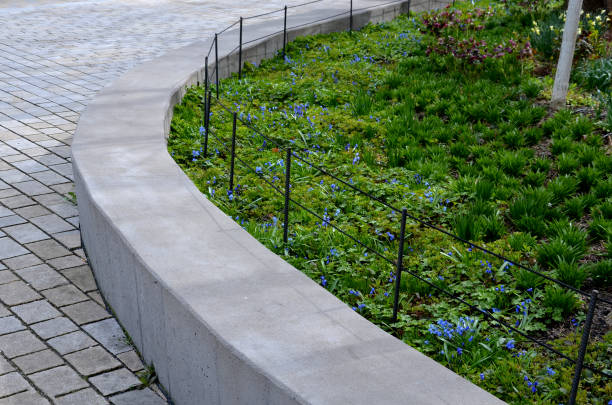 純粋な鋳造コンクリートで作られた座席の壁を保持すると、その後ろに紫色の花が咲き、壁はentrancに対して黒いロープを持つ金属製のフェンスで囲まれています - landscaped retaining wall wall stone ストックフォトと画像